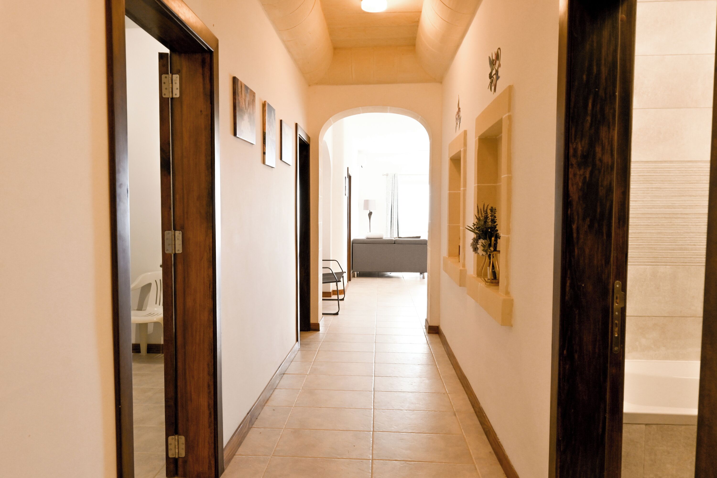 Un corridoio con pavimento piastrellato, porte in legno e quadri appesi alle pareti.