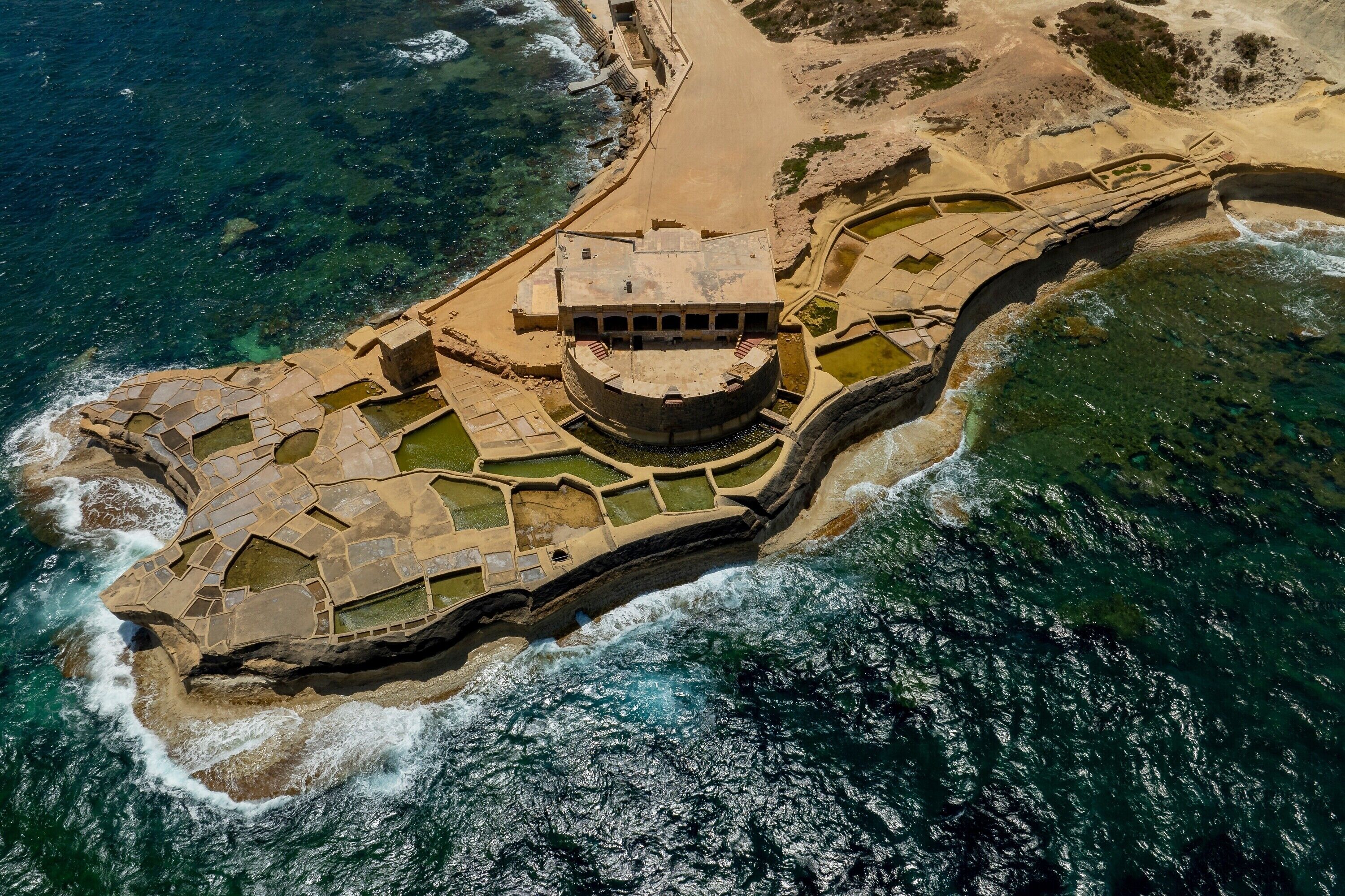 An aerial view of a coastal fort with a central courtyard, surrounded by walls and a beach.