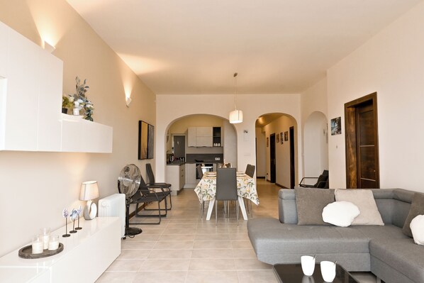 A modern living room with a grey sofa, a dining table with chairs, and a kitchen in the background. - Sea & Valley Views Żebbuġ Gozo (Zebbug)