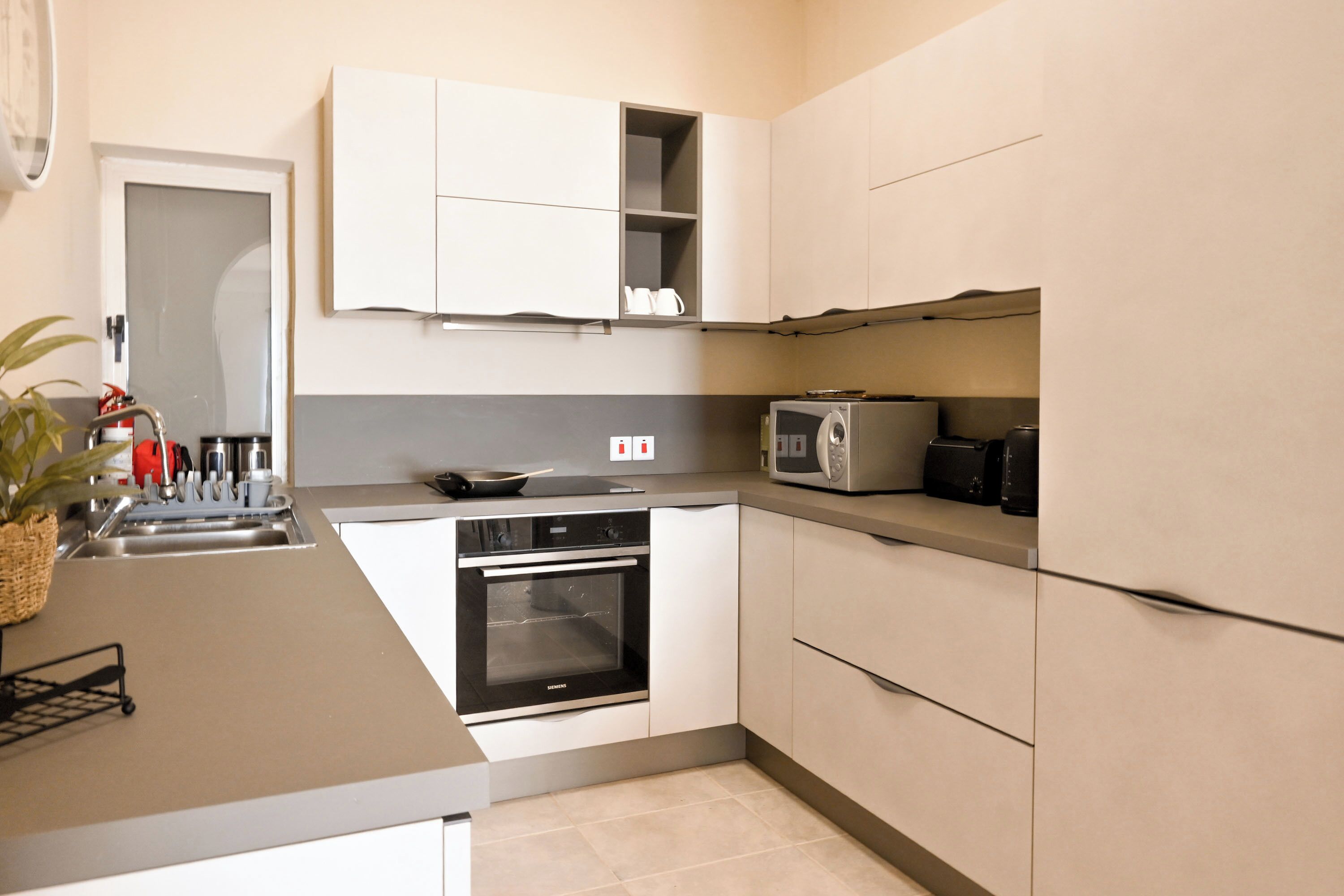 A compact kitchen with white cabinets, a built-in oven, a microwave, and a sink.