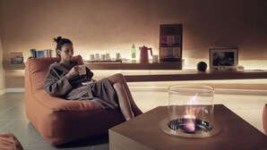A person sitting on a brown sofa in a room with a glass table in front of them, a fireplace, and various items on shelves in the background. - San Colombano Suite (Bardolino)
