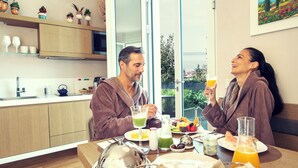 A modern kitchen with wooden cabinets, a dining table set with breakfast, and a view of the outdoors. - San Colombano Suite (Bardolino)