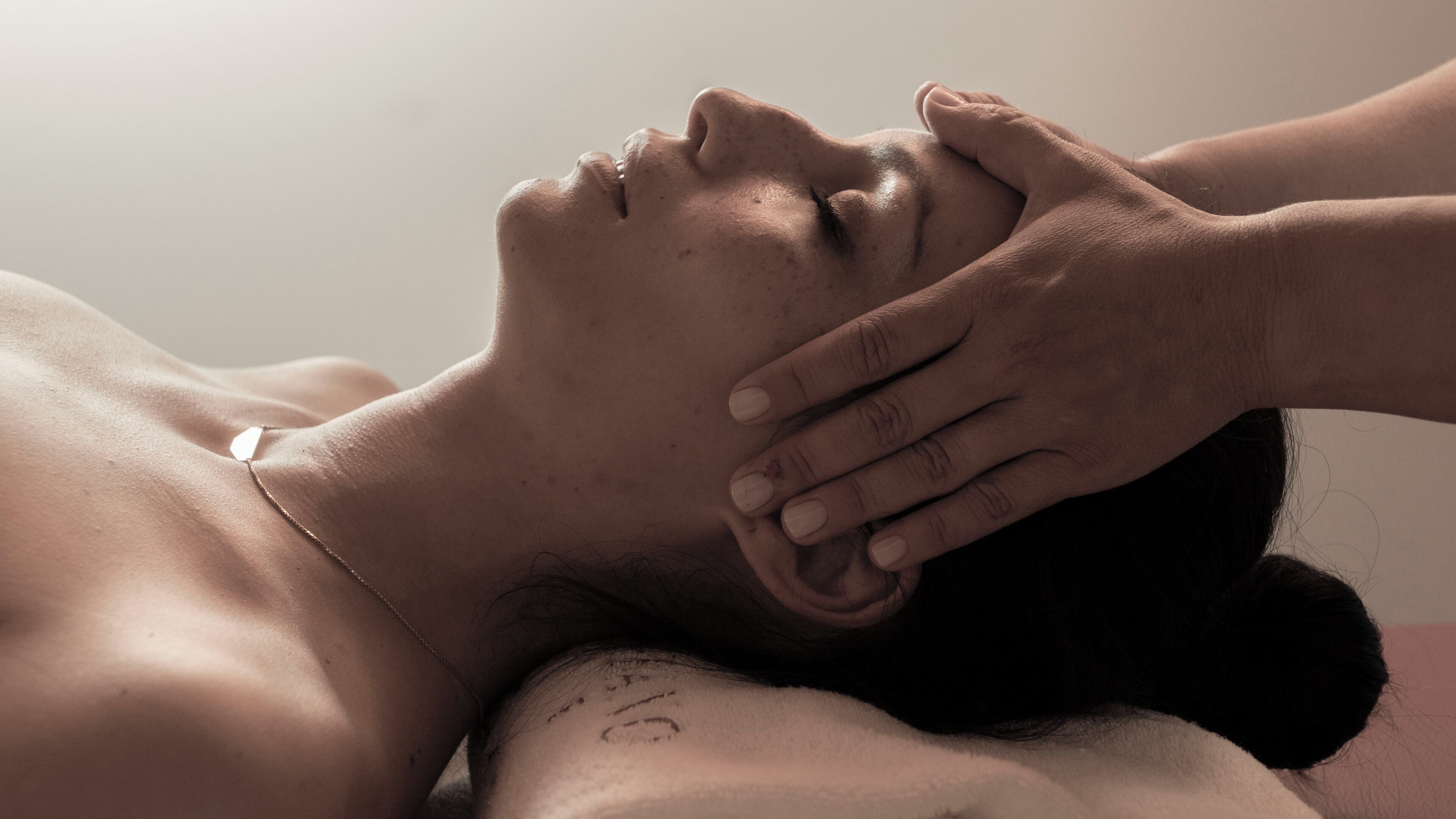 Une personne est allongée, la tête reposant sur une surface, et une autre personne lui touche la tête.