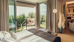 A bedroom with a large bed, a view of a balcony with a person sitting, and a vase with feathers. - San Colombano Suite (Bardolino)