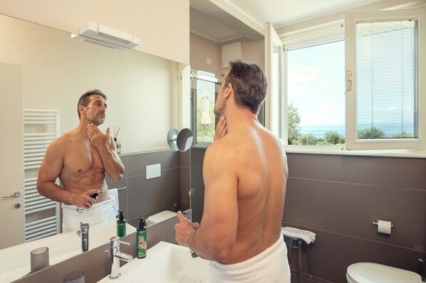 Un hombre en un baño con un espejo grande, una toalla y artículos de tocador sobre el mostrador.