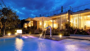 A modern hotel with a swimming pool, outdoor seating, and a well-lit facade. - San Colombano Suite (Bardolino)