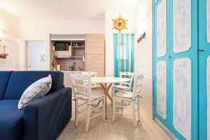 Un espace de vie compact comprenant un canapé bleu, une table à manger avec des chaises, un coin cuisine et une grande porte bleue.