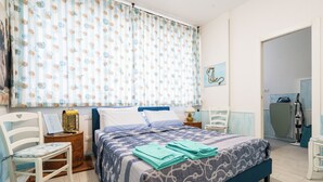 A bedroom with a bed, a chair, a nightstand, a lamp, and a window with curtains.