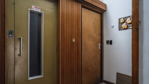 A wooden door with a vertical window, a doormat, and a wall-mounted light switch.