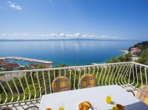 A balcony with a table set for breakfast, overlooking a marina and a calm sea. - Sea View Apartments Lendic Podgora (Podgora)
