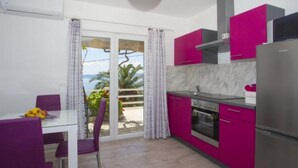 A modern kitchen with pink cabinets, a white dining table with purple chairs, and a view of the sea through the sliding glass doors. - Sea View Apartments Lendic Podgora (Podgora)