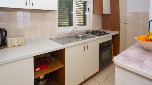 A compact kitchen with white cabinets, a sink, a stove, and a window with blinds. - Sea View Apartments Lendic Podgora (Podgora)