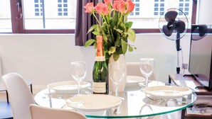 A dining area with a glass table, white chairs, and a vase of flowers. - Stunning Studio - Sleeps 4 (Staines)