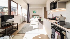 A modern kitchen with a flat-screen TV, a microwave, and a toaster. There is a dining area with a table and chairs, and a large window providing a view of the city. - Stunning Studio - Sleeps 4 (Staines)