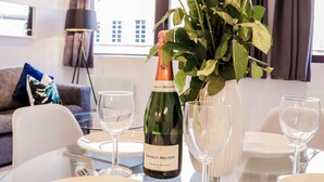 A dining table with a vase of flowers, a bottle of wine, and empty wine glasses. - Stunning Studio - Sleeps 4 (Staines)