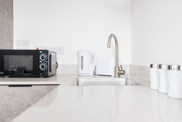 A modern kitchen with a microwave, kettle, and stainless steel sink. - Modern 1 Bed Flat in Town Centre - Free Wifi (Luton)