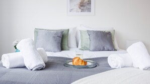 Una cama bien hecha con ropa de cama blanca y gris, dos almohadas y una bandeja con un croissant y un vaso de agua.