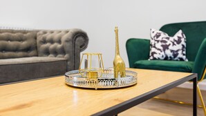 A modern living room with a grey tufted sofa, a green armchair with a patterned pillow, and a wooden coffee table with a decorative tray. - Modern 2 bed Flat in Town Centre - Free Wifi (Luton)