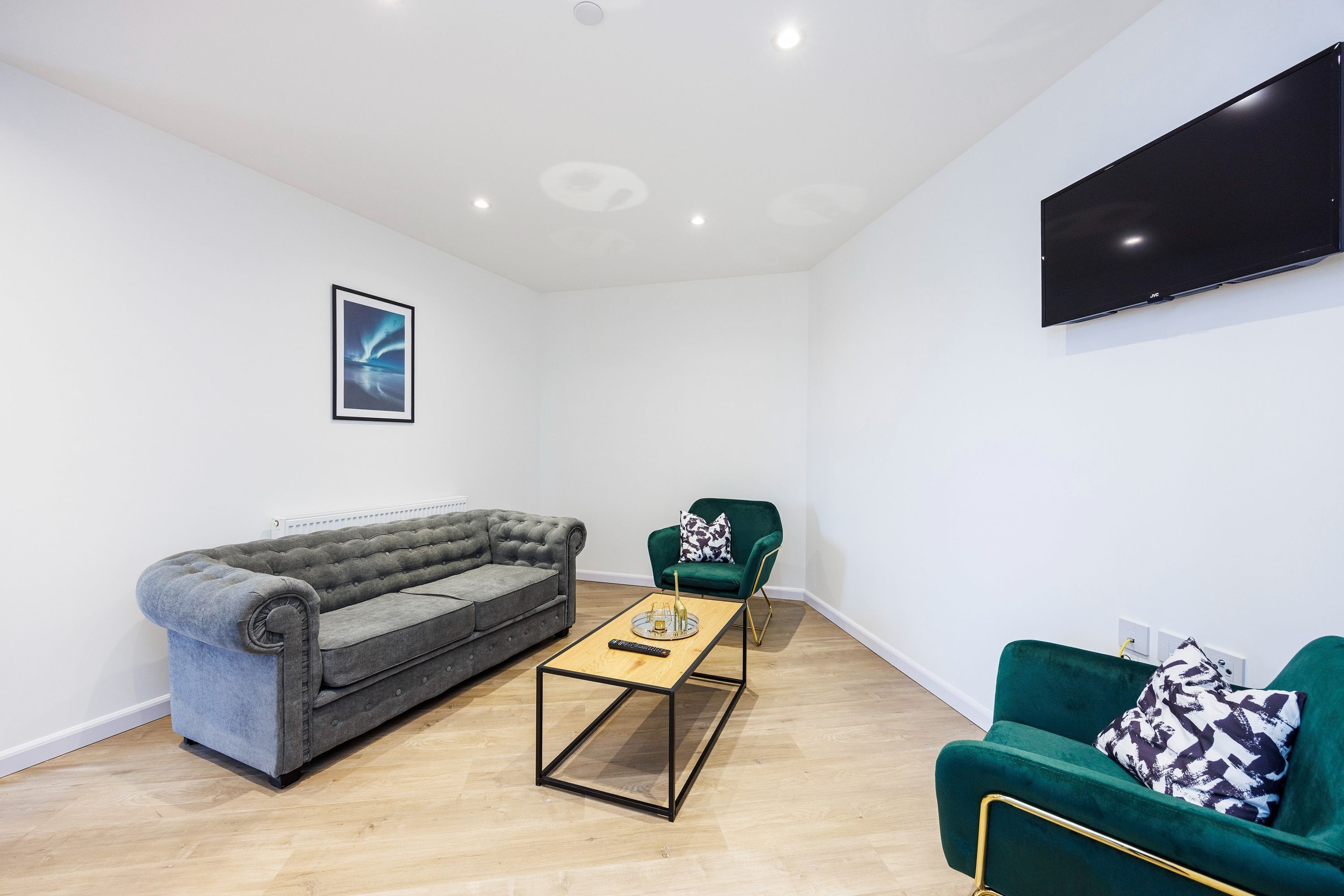 Ein modernes Wohnzimmer mit einem grauen, gesteppten Sofa, einem grünen Sessel, einem Holztisch und einem flachbildfernseher, der an der Wand montiert ist.
