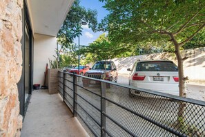 A parking area with several cars, a metal fence, and a building with a brick facade. - Bright Tulum 2BR - Rooftop Pool near Aldea Zama (Tulum)