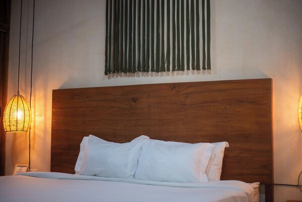 Un lit bien fait, avec du linge de lit blanc, une tête de lit en bois et deux lampes fixées au mur.