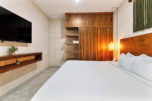 Een moderne hotelkamer met een groot bed, een houten garderobe, inbouwplanken, een flatscreen televisie en een bedlampje.