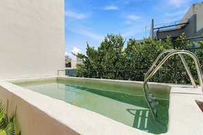 Ein Pool auf dem Dach mit einer Metallleiter, umgeben von einer weißen Mauer und einem Metallgeländer.