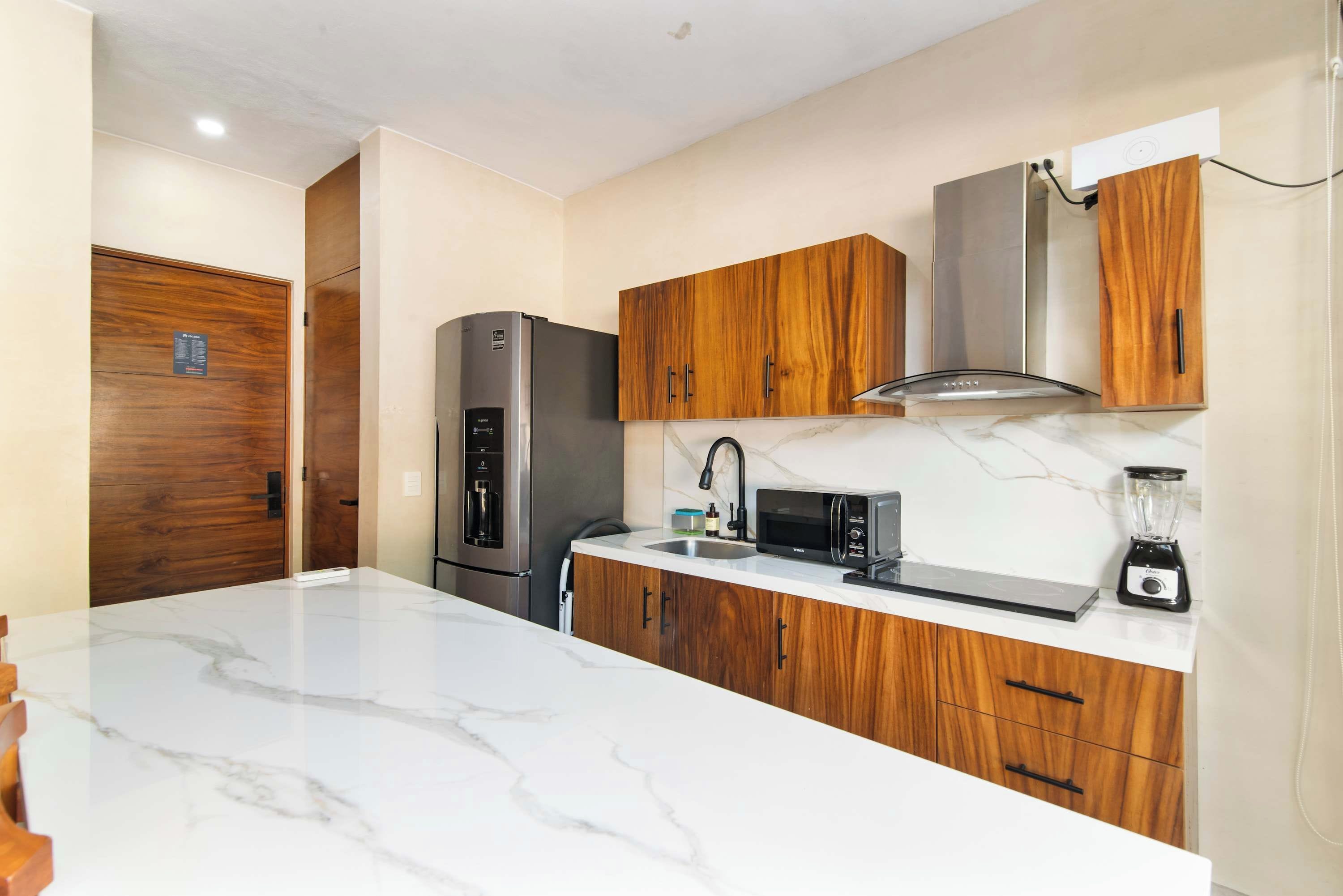 A modern kitchen with marble countertops, wooden cabinets, stainless steel appliances, and a built-in microwave.