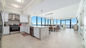 A modern kitchen with a central island, stainless steel appliances, and a view to the outside. - New Complex!  Beachfront 4BR, Lazy River and Water Slide! (Gulf Shores)