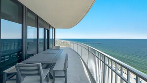 A balcony with a table and chairs, overlooking a beach and the ocean. - New Complex!  Beachfront 4BR, Lazy River and Water Slide! (Gulf Shores)