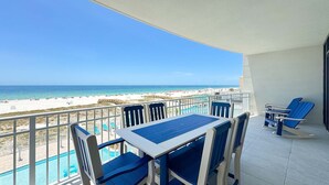 A balcony with a table and chairs, overlooking a beach and a clear blue sky.