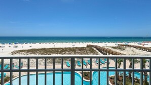 A beach view with a pool area, lounge chairs, and a wooden deck.