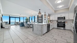 A modern kitchen with white cabinetry, a central island, and a view to the outside. - New Complex!  Beachfront 4BR, 5TH FLOOR!, Lazy River and Water Slide! (Gulf Shores)