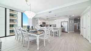 Une cuisine moderne avec des meubles blancs, un îlot central et un coin repas avec des chaises blanches.