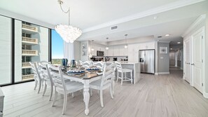 Una cocina moderna con armarios blancos, una isla central y un comedor con sillas blancas.
