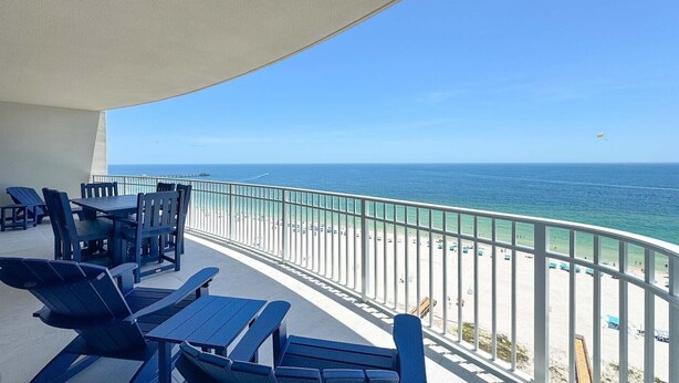 Un balcon avec des chaises et des tables bleues, donnant sur une plage et l’océan.