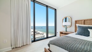 Une chambre avec une grande fenêtre, un lit, une table de chevet, une lampe et un miroir.