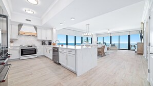 Une cuisine moderne avec des meubles blancs, un îlot central et une vue sur la mer grâce à de grandes fenêtres.