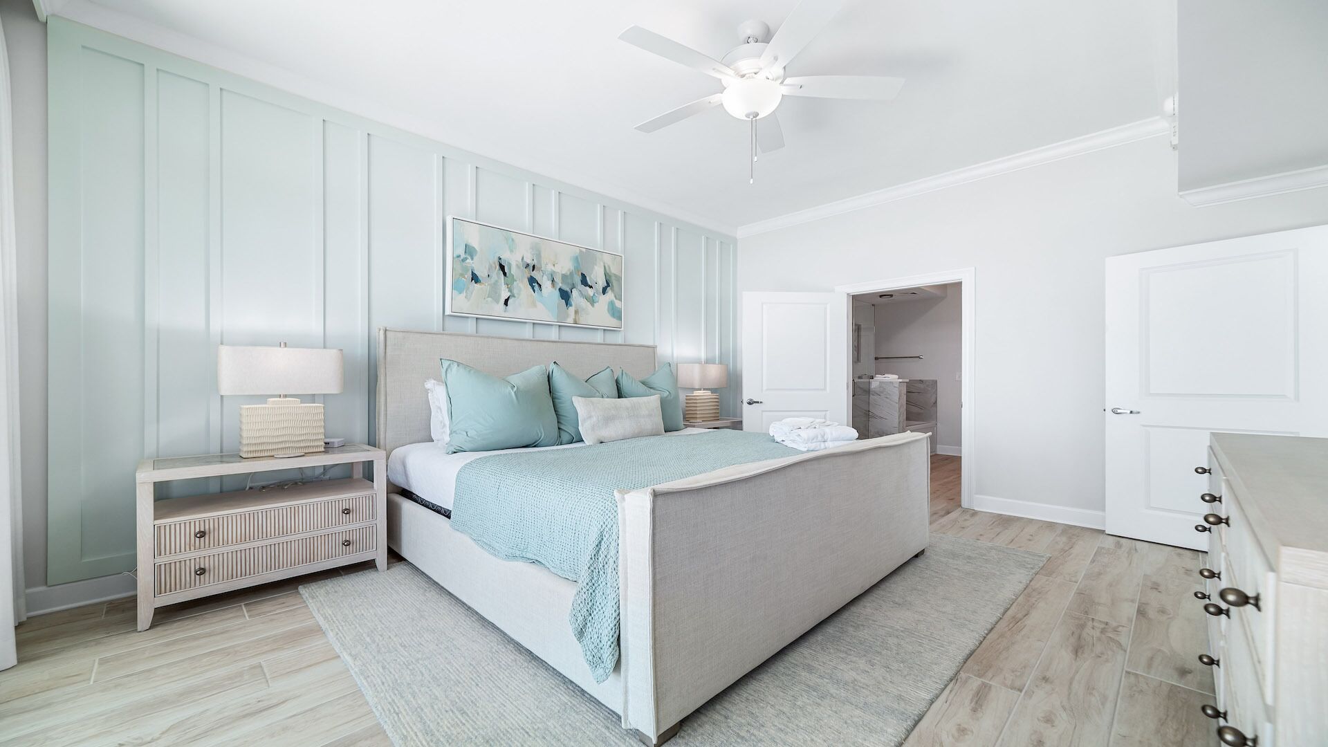 A bedroom with a bed, nightstands, a ceiling fan, and a door leading to a bathroom.