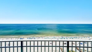 A beach with clear blue waters, a sandy shore, and a metal railing in the foreground. - New Complex!  Beachfront 4BR Beauty! Lazy River and Water Slide! (Gulf Shores)