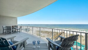 Een balkon met uitzicht op het strand, met een tafel, twee glazen en meerdere stoelen.