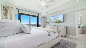 A bedroom with a large bed, a ceiling fan, a TV, and a view of the ocean. - New Complex! Beachfront 3BR, 3RD FLOOR, LAZY RIVER AND WATER SLIDE!! (Gulf Shores)
