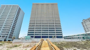 Un grand hôtel moderne doté de nombreux balcons, une promenade en bois menant à l’entrée et un ciel d’un bleu limpide.
