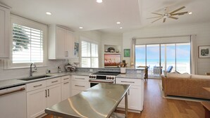 Una cocina moderna con armarios blancos, una isla de acero inoxidable y un amplio ventanal con vistas a la playa.