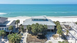 Una propiedad frente a la playa con una casa grande, varias palmeras y una playa de arena.