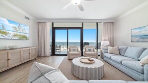 A spacious living room with a large sliding glass door leading to a balcony with a view of the beach. There are two armchairs, a sofa, and a coffee table with decorative items. - New Complex!  Beachfront 3BR! 4TH FLOOR!!  LAZY RIVER and WATER SLIDE!! (Gulf Shores)