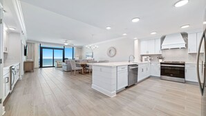 A modern kitchen with white cabinetry, a central island, and a view to the outside. - New Complex!  Beachfront 3BR! 4TH FLOOR!!  LAZY RIVER and WATER SLIDE!! (Gulf Shores)