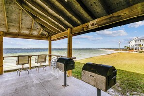 Un espace extérieur abrité avec vue sur l’eau, deux barbecues et une table avec des chaises.