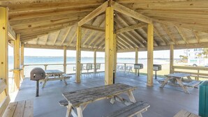 Ett avskärmat område på stranden med picknickbord och bänkar i trä, en brevlåda och utsikt över havet.