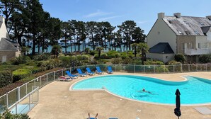 Una piscina con borde curvo, rodeada de sillas reclinables azules y una cerca blanca.